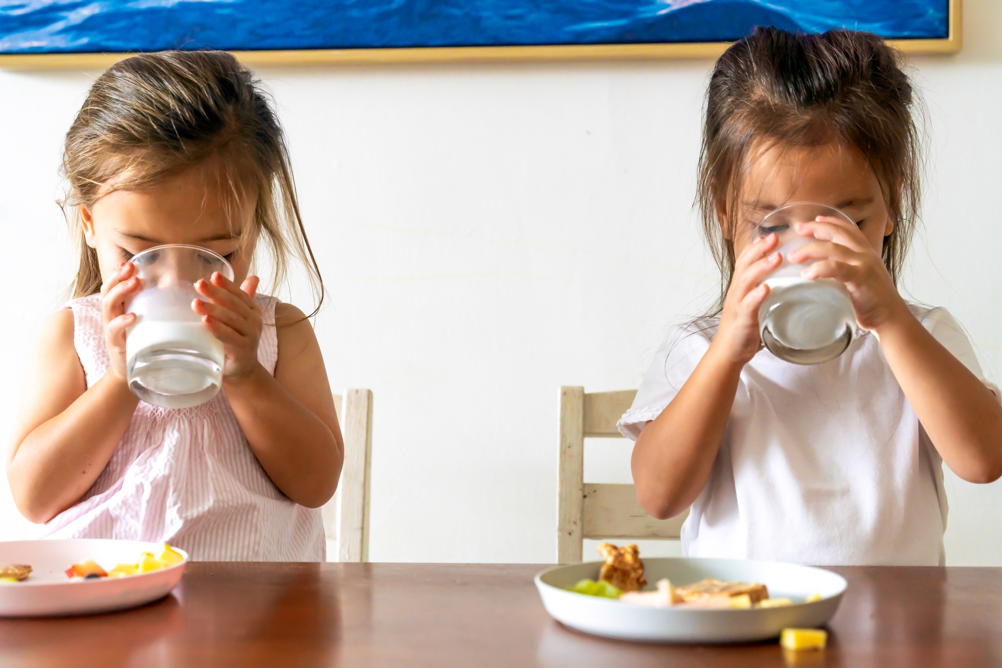 Two little girls having their glass of milk with a plate of healthy snacks laid out on the table